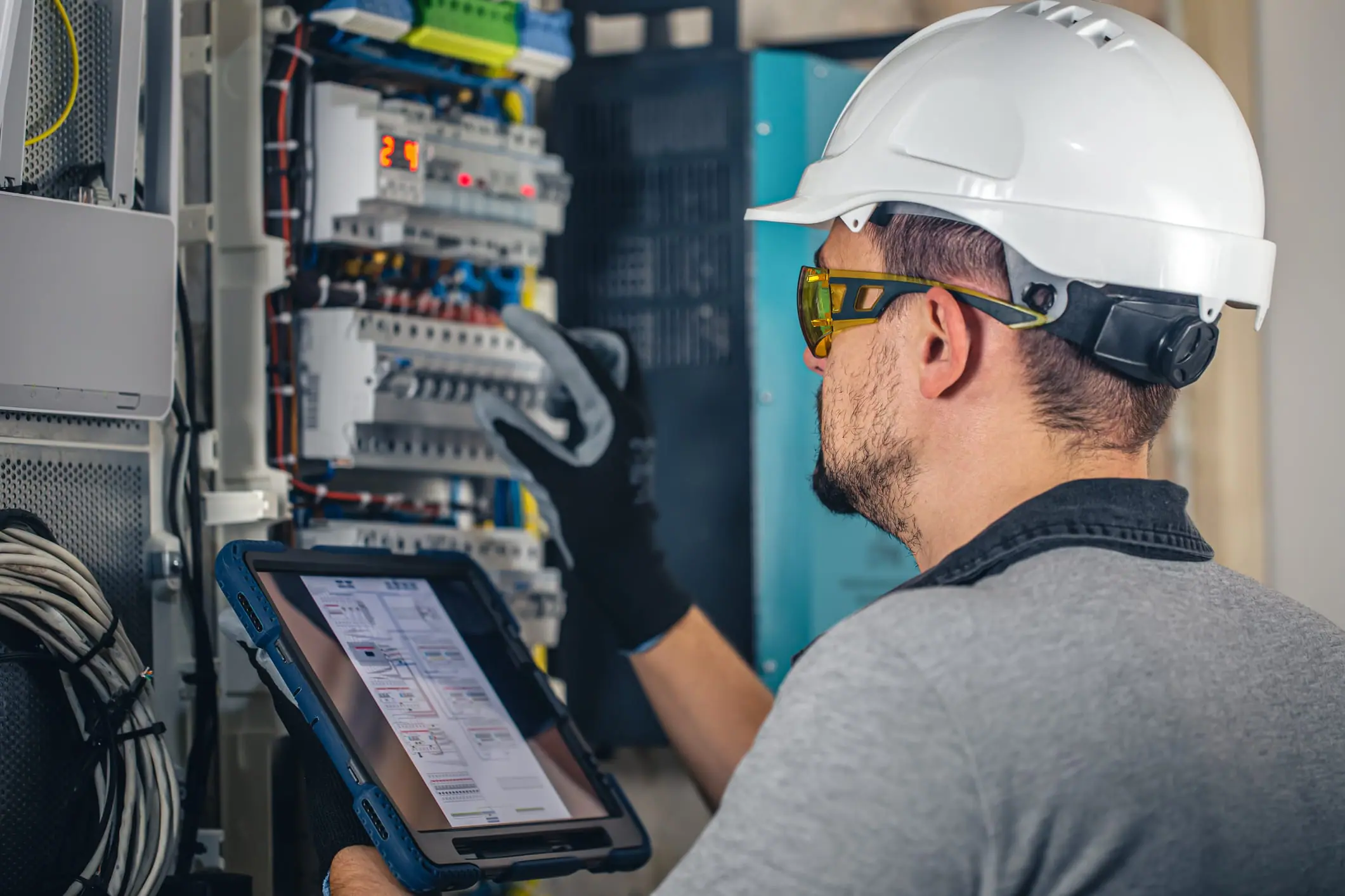 Man, an electrical technician working in a switchboard with fuses, installation and connection of electrical equipment. A professional uses a tablet - what is a protective relay. 